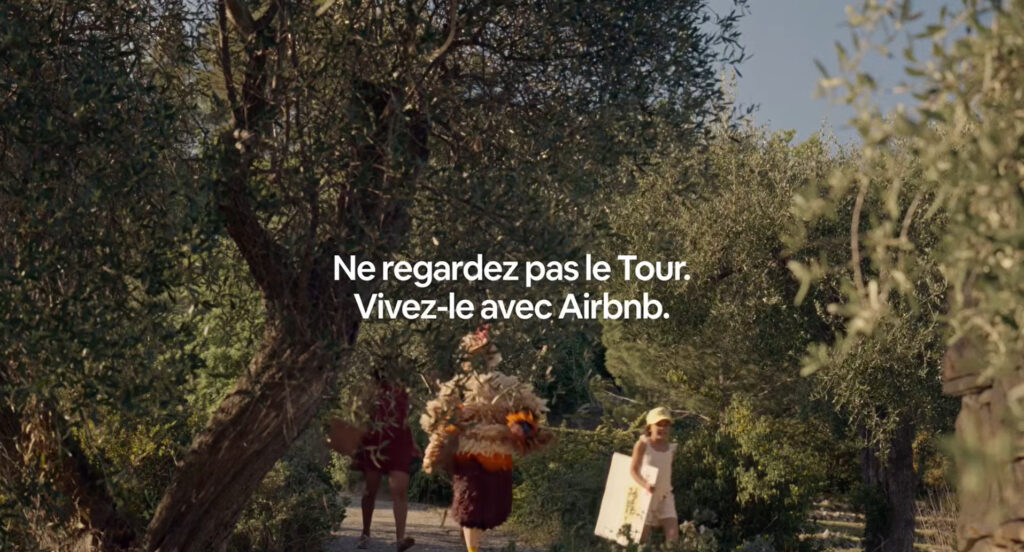 How Airbnb Made Itself French: The Tour de France, 90 Years of Paid Vacations, and Zero Ads About Paris 2 A family cheers on passing cyclists from the roadside in a screenshot from the 2026 Airbnb Tour de France TV commercial.